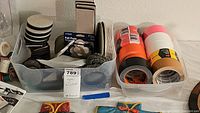 Plastic bins with furniture slide pads and multiple rolls of assorted tapes including duct tape and gorilla tape in various colors