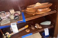 Wooden carved bowls, several ocarinas including a painted ceramic horse-shaped flute, colorful wooden ocarina, small hanging ornaments, and polished stones on wooden shelves.