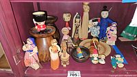 Shelf display of diverse vintage ethnographic wooden, straw, and fabric dolls, including kokeshi style and amigurumi dolls