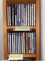 Music CD collection on wooden rack, first and second shelves, mostly classical music discs with titles such as Bach and Handel.