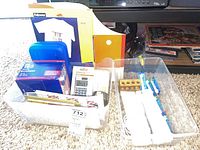 Clear bins displaying the toothbrush, replacement heads, calculator, envelopes, folders, blue organizer case, and box of staples