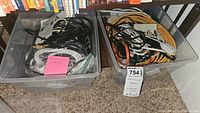Two large plastic bins filled with various cables and cords placed on carpet near a bookshelf.
