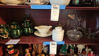 Wide shelf view showing multiple glass and ceramic items including green gilt collection, white gravy boat, and etched glass pieces.