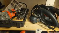 Photo of Black & Decker fingertip sander FS540 in its black plastic case with manual, and Black & Decker Wood Hawk circular saw model C2020 type 1, cords coiled, on wooden shelf