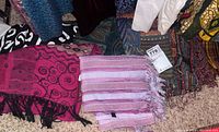 Scarves laid out on carpet showing patterns and colors including a pink scarf with black swirls and a striped pink-purple scarf.