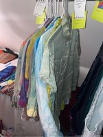 Side view of hanging indigo dyed silk shirts and blouses on plastic hangers showing color variations and textures