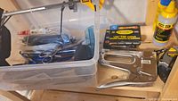 Photo of plastic container with hand tools inside, heavy staple gun and box of staples on wooden surface