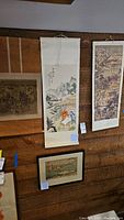View of four art pieces: two vertical Japanese scrolls, one framed print below, and one bamboo scroll horizontally placed. Shows general display and condition.