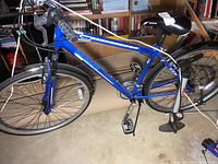 Side view of blue CCM men's 18-speed hybrid bike with pumping included alongside on floor.