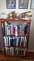 Front view of wooden bookshelf filled with books and decorative airplane models on top, showing scratches on surface.