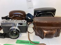 Konica camera with Hexanon lens beside multiple protective camera cases on a white background