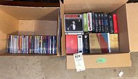 Two open cardboard boxes with a total of about 30 CDs, mostly sealed, placed vertically showing spines distinct in text and colors.
