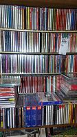 Four shelves densely packed with music CD jewel cases and loose stacks in front.