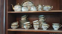 Porcelain tea set shelves with teapot, creamers, sugar bowl, teacups and saucers showing hand painted floral and bird detail with gold trim