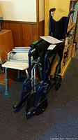 Blue folding medical wheelchair with fabric seat and backrest, positioned standing upright with manual placed on seat.