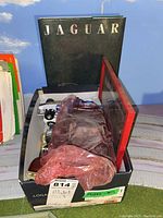 Photo of box with various model cars inside, covered in plastic, including visible white and dark colored models.