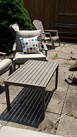 Photo of outdoor armchair and matching rectangular table on stone patio. Chair has beige cushions and polka dot lumbar pillow.