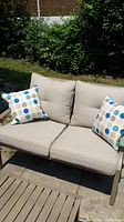 Front angle showing beige cushions and two printed throw pillows on the loveseat.