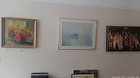 Three framed artworks visible on beige wall including floral painting and two prints