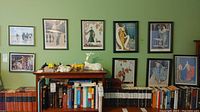 Wide view of six framed prints hung above a wooden table, featuring various fashion-themed artworks