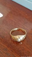 Ring placed on wooden surface showing top patterned textured design, highlighting its gold color and swirled motif.