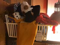 White laundry basket with hats including brown and blue checkered hat, furry paw-style hat with a pompom, and red T-shirt