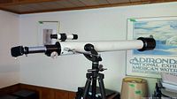 Full side view of white Tasco refractor telescope on black tripod.