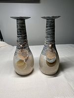 Front view of two ceramic candle holders with shells tied around the neck.