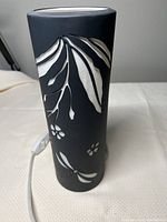 Side view of the lamp showing black matte finish and white floral cutouts.