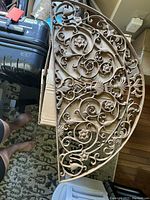 Top view of the decorative cast metal half circle floor grate showing detailed floral and scrollwork design, positioned on cardboard.