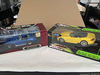 Two boxed diecast metal car models on table; left: blue 40th Anniversary Cobra, right: yellow 2003 Dodge Viper SRT-10 Fast and Furious edition.