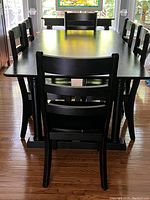 Front-on view of the rectangular black painted dining table surrounded by six matching chairs arranged three per side.