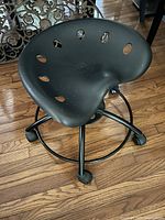 Side perspective showing molded plastic seat with ventilation holes, metal base with footrest and castors on wood floor.
