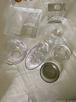 Photo showing multiple clear glass items including square and round bowls, some with etched floral patterns and one tinted bowl.
