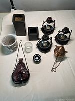Full view of all items on a table showing the purple glass bottle in metal hanger, three spherical glass lanterns in black metal frames, copper hanging lantern, various ceramic and wood-look vases, and tea light holders.