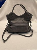 Front view of the gray leather bag displaying the drop handles, front zippered pocket, and metal chain crossbody strap.