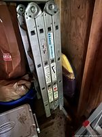 Side view of Krause MultiMatic folding ladder folded and leaning in storage, showing branding and warnings.