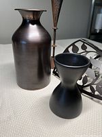 Photo showing dark metal vase and two candle holders with visible finishes and shapes.