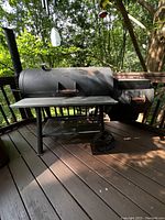 Full view of the black steel Oklahoma Joe horizontal charcoal grill and smoker showing the main cooking chamber with a front shelf, attached firebox, wheels, and legs.