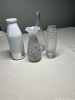 All four small vases grouped on a white surface including white and clear vases with various shapes and patterns.
