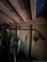 Photo showing the entire Troy-Built 27cc 2-stroke weed eater hanging in a wooden shed with some tools and a ladder underneath it.