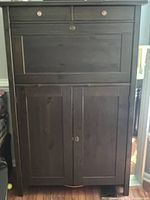 Front view of closed dark wood cabinet showing two drawers with glass knobs and lockable lower doors.