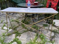 Front-side angle showing the rectangular marble top, some cracks visible, supported by gold-colored metal rod base.