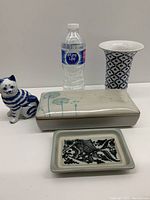 Front view of four vintage decorative items with water bottle for scale: cat figurine, covered box, small tray, and blue and white vase.