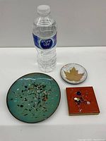 Photo of all three enamel plates/plaques with a water bottle to show scale