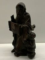Front view of vintage Asian stone carving showing male figure holding a scroll and child figure attached at side, with visible breaks and scratches.