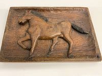 Front view showing carved horse in relief with textured mane and tail on wooden rectangular plaque.