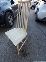 View of one wooden chair angled to show high spindle back, curved seat, and leg structure on pavement.