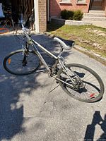 Photo of a silver 28-inch Infinity bicycle outside in daylight against a driveway and brick wall background.