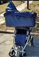 UPPAbaby stroller frame with dark blue bassinet attached, photographed outdoors on concrete with shadow showing the frame details and wheels.